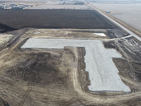 Aerial view of construction site with large L shaped building pad with Waukee in the distance