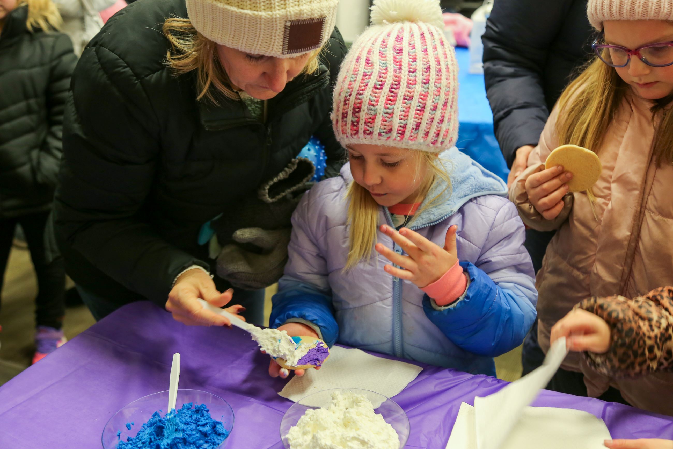 Adult helping young girl frost a sugar cookie