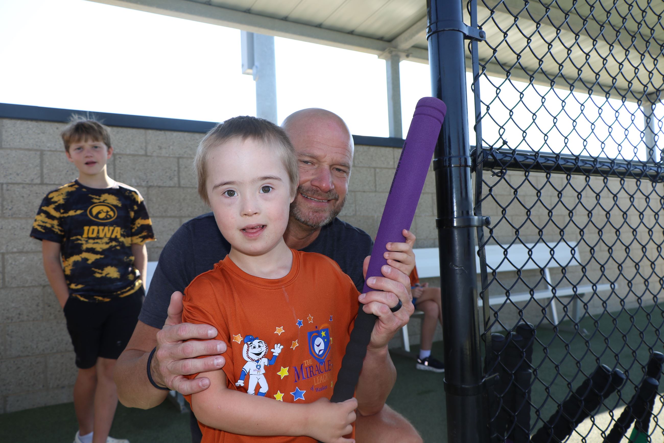young player with a foam bat and a volunteer in the dugout