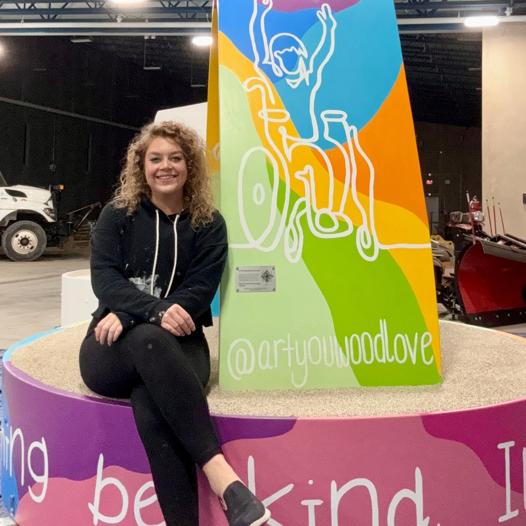 Woman with curly hair sitting on bright neon colored bench that she painted